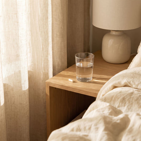 A glass of water and a single capsule on a bedside table
